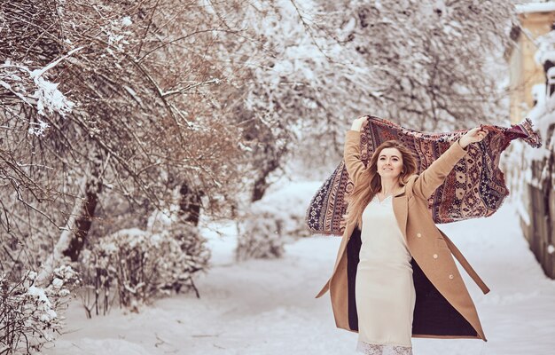 Belle fille se tient avec foulard flottant dans le vent dans un parc d'hiver