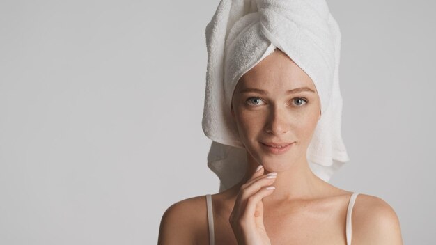 Belle fille avec une serviette sur la tête regardant sensuellement à huis clos sur fond blanc. Place pour la publicité ou le texte promotionnel
