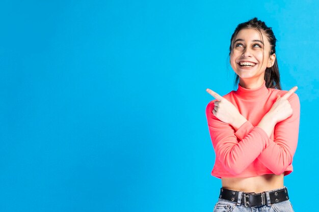 Une belle fille souriante croise les mains et pointe les doigts vers l'extérieur