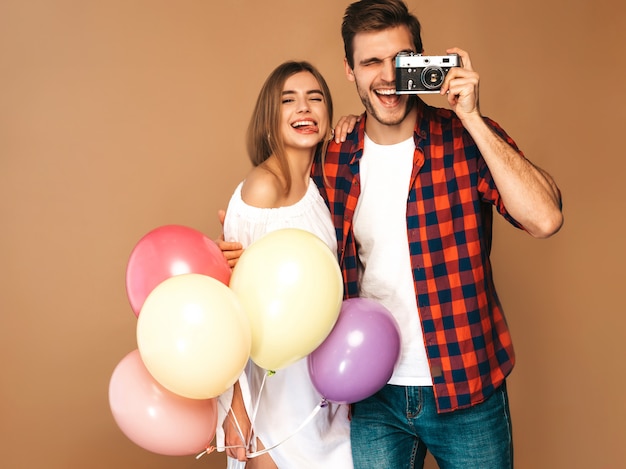 Belle fille souriante et son beau petit ami tenant des tas de ballons colorés. Couple heureux, prendre des photos d'eux-mêmes sur appareil photo rétro. Bon anniversaire