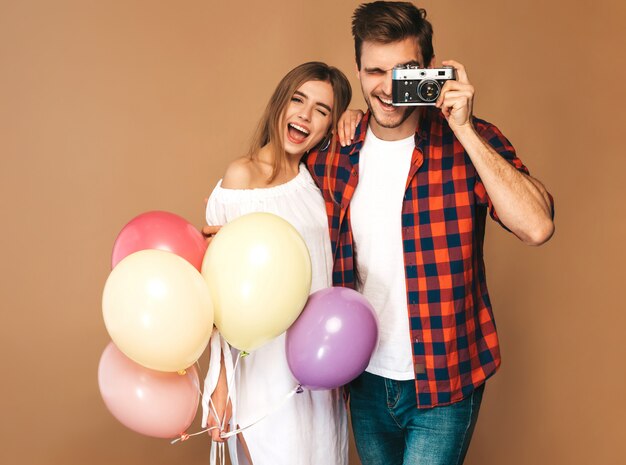 Belle fille souriante et son beau petit ami tenant des tas de ballons colorés. Couple heureux, prendre des photos d'eux-mêmes sur appareil photo rétro. Bon anniversaire