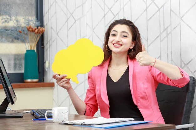 Belle fille tenant une bulle d'idée jaune en forme de nuage et gestes pouce vers le haut Photo de haute qualité