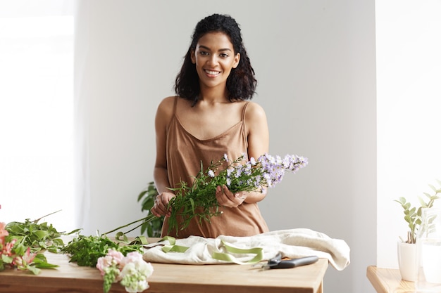 Belle fleuriste femme africaine souriant tenant des fleurs. Mur blanc. Propriétaire d'entreprise heureux de rencontrer des clients.