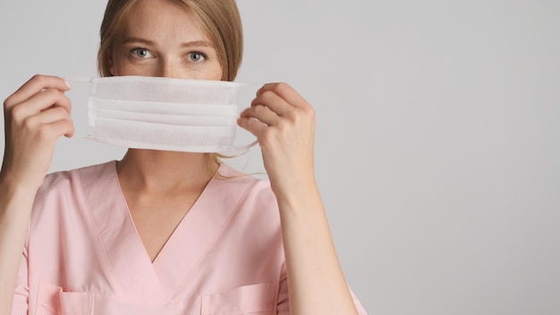 Belle infirmière blonde portant un masque médical devant la caméra avec place pour publicité ou texte promotionnel près sur fond blanc