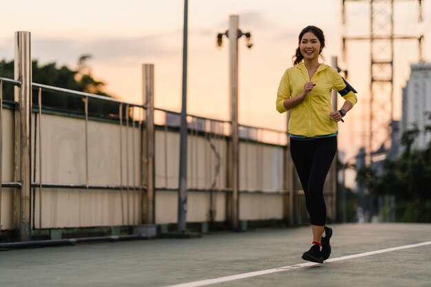 Belle jeune athlète d'Asie exécutant des exercices d'entraînement en milieu urbain. Teen girl japonaise portant des vêtements de sport sur le pont de la passerelle en début de matinée. Mode de vie sportif actif en ville.