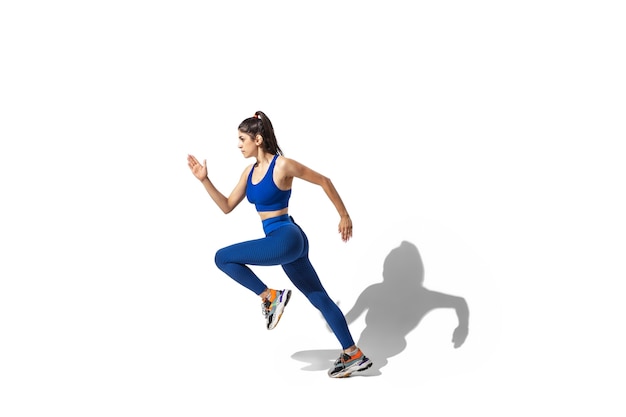 Belle Jeune Athlète Féminine Pratiquant Sur Fond De Studio Blanc, Portrait Avec Des Ombres. Modèle De Coupe Sportive En Mouvement Et En Action.