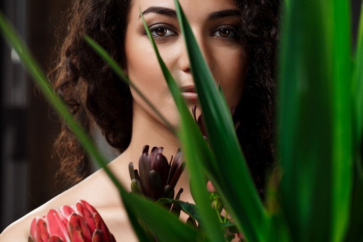 Photo gratuit une belle jeune brune dans des plantes tropicales sur un mur gris