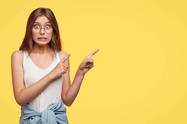 Belle jeune brune avec des lunettes posant contre le mur jaune