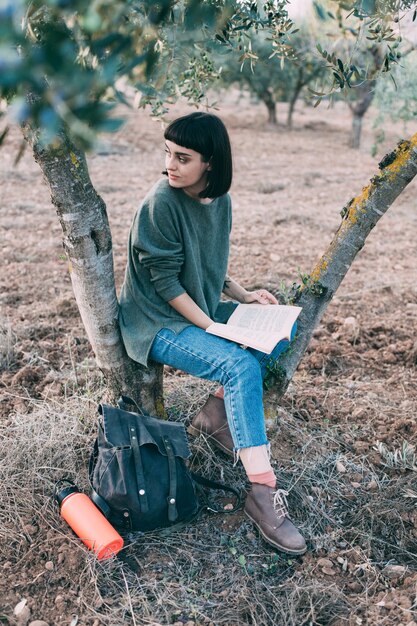 Belle jeune brune s'asseoir sous l'arbre lire livre