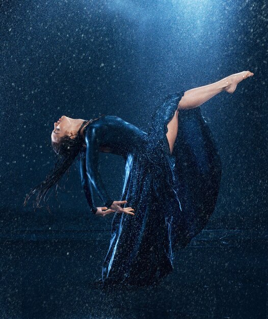 La belle jeune danseuse moderne danse sous des gouttes d'eau