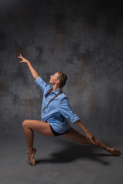 La belle jeune danseuse de style moderne dans une chemise bleue posant sur un fond gris studio