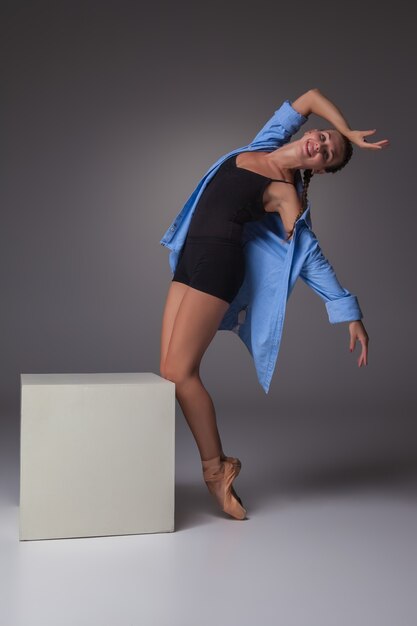 La belle jeune danseuse de style moderne posant sur un cube blanc sur un fond gris studio