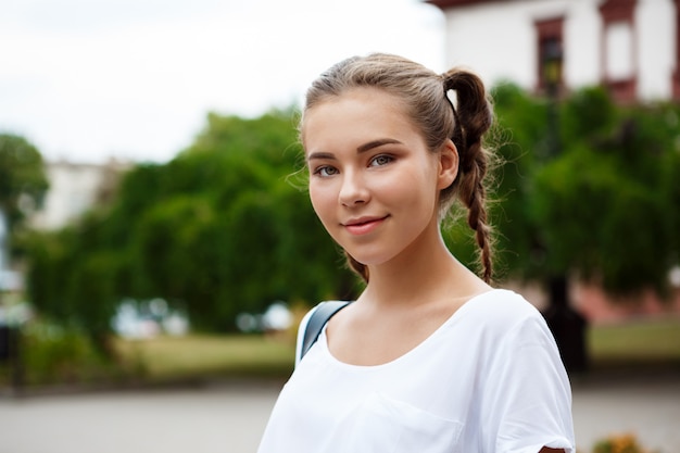 Belle jeune étudiante joyeuse souriante, tenant des dossiers à l'extérieur.