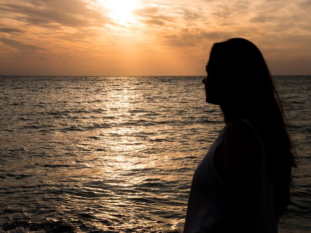 Belle jeune femme admirant le coucher de soleil sur la mer. Belle femme réunie avec la nature