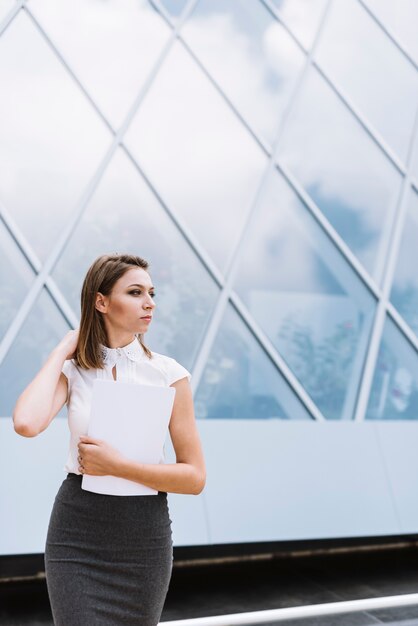 Belle jeune femme d&#39;affaires détenant du papier de document dans la main à la recherche de suite