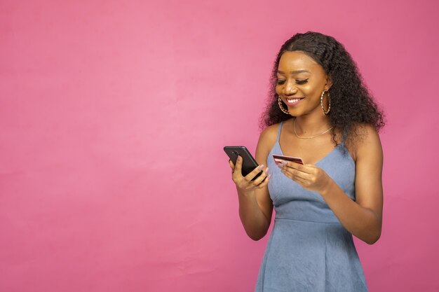 Belle jeune femme africaine à l'aide de son téléphone portable et de sa carte de crédit