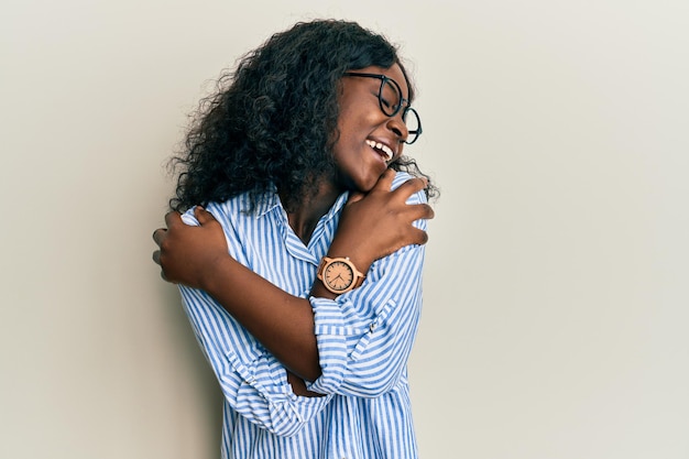 Photo gratuite belle jeune femme africaine portant des vêtements décontractés et des lunettes se serrant dans ses bras heureux et positif, souriant confiant. amour de soi et soin de soi