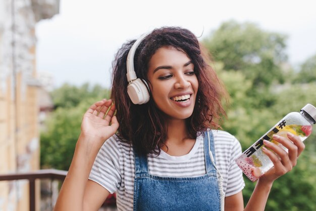 Belle jeune femme africaine sans maquillage s'amusant avec de la musique préférée en plein air