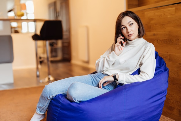 Belle jeune femme à l'aide de son téléphone tout en étant assis dans un sac de chaise