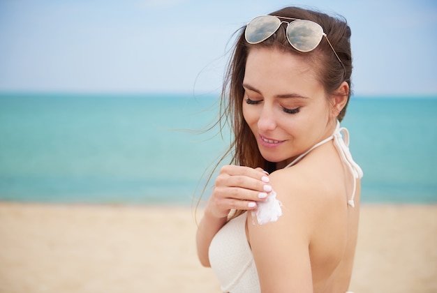Belle jeune femme appliquant la crème solaire sur la plage