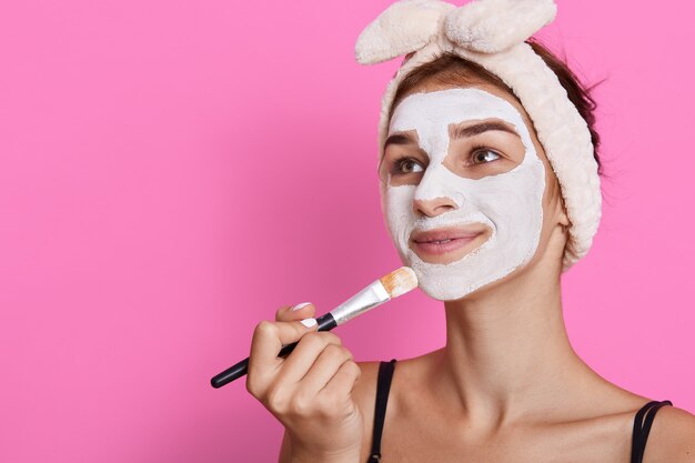 Belle jeune femme appliquant un masque facial à la maison