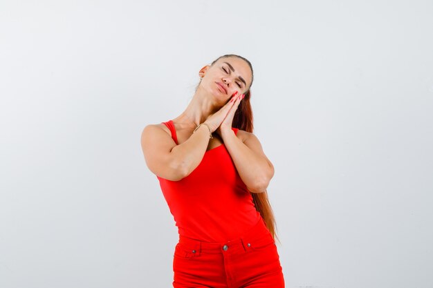 Belle jeune femme appuyée sur les paumes comme oreiller en débardeur rouge, pantalon et à la vue de face, paisible.