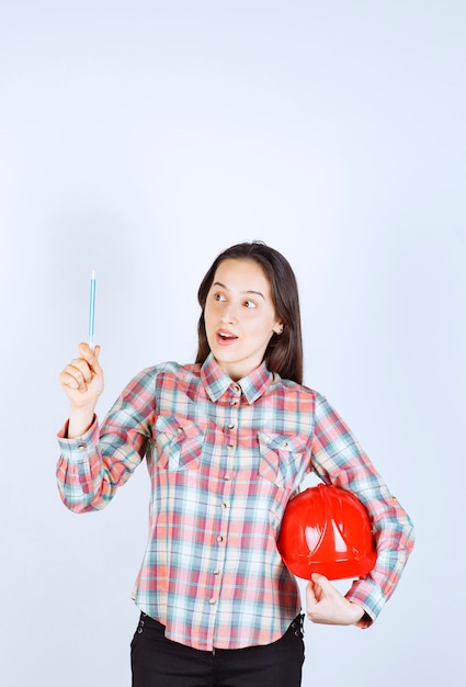 Belle jeune femme architecte tenant un casque de sécurité avec un stylo.