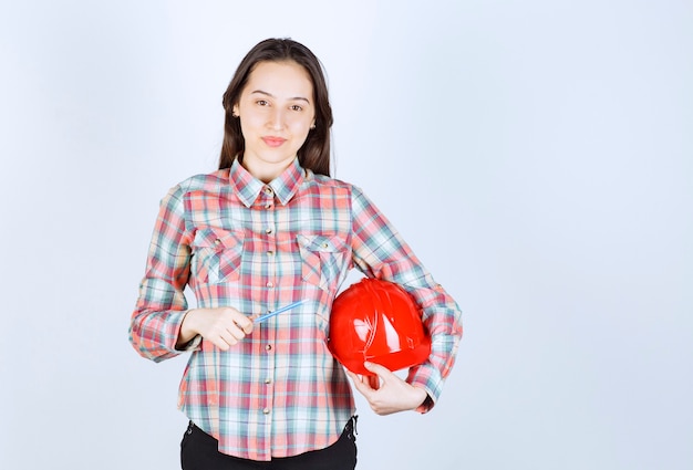 Belle jeune femme architecte tenant un casque de sécurité avec un stylo.