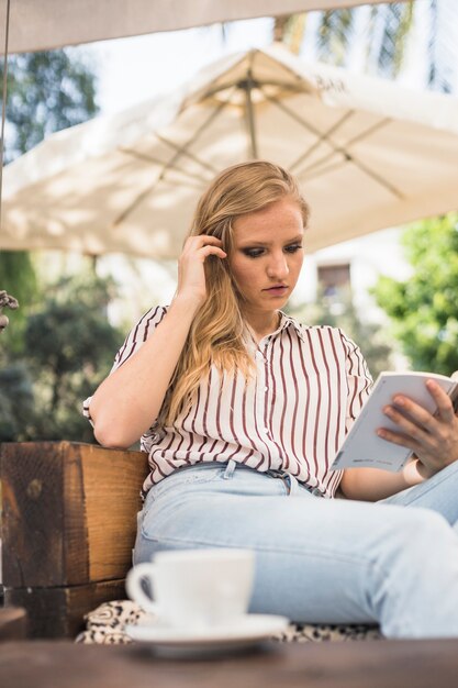 Belle jeune femme assise sur le canapé, lecture de livre à l&#39;extérieur