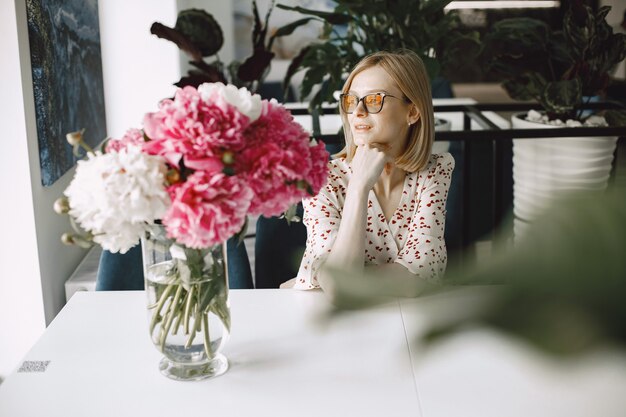 Une belle jeune femme assise dans un café à l'intérieur et buvant du café. Femme portant des lunettes et une robe à fleurs