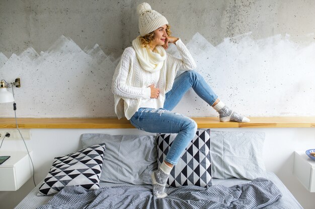 Belle jeune femme assise dans la chambre contre le mur portant un pull blanc