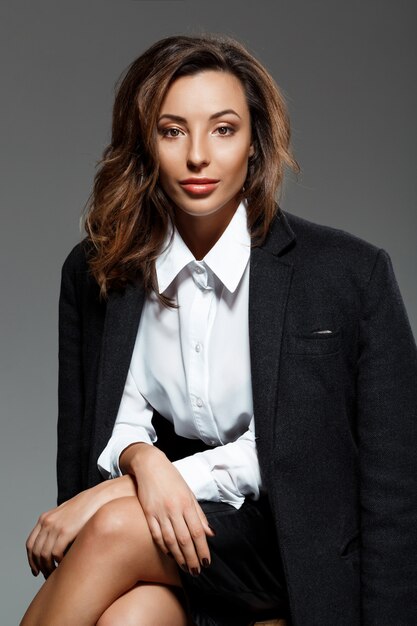 Belle jeune femme assise sur un mur gris