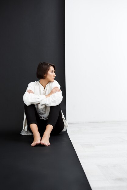 Belle jeune femme assise sur le sol sur une surface en noir et blanc