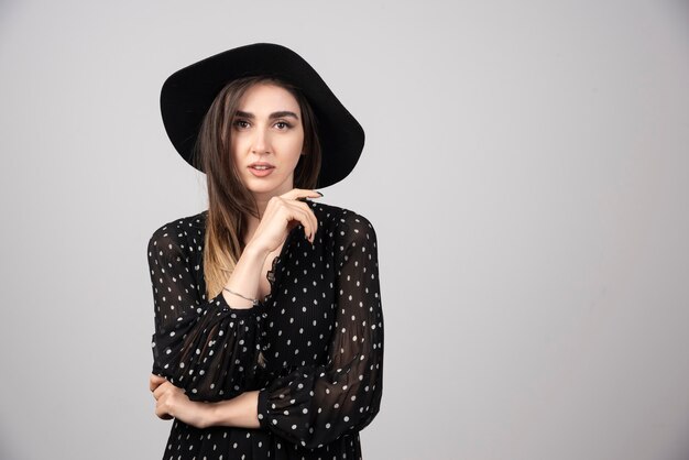 Belle jeune femme au chapeau noir debout les bras croisés.