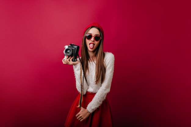 Belle jeune femme au chapeau rouge faisant des grimaces tout en posant avec la caméra