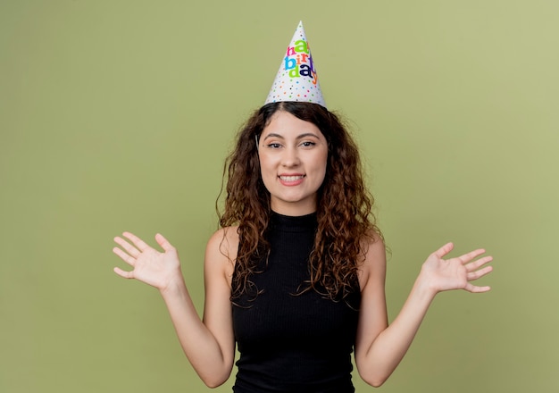 Photo gratuite belle jeune femme aux cheveux bouclés dans un chapeau de vacances concept de fête d'anniversaire heureux et excité debout sur un mur léger