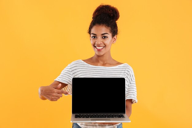 Belle jeune femme aux cheveux bouclés montrant un ordinateur portable isolé