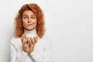 Photo gratuite belle jeune femme aux cheveux rouges, tient une tasse de thé blanc, a parlé avec un interlocuteur tout en buvant une boisson chaude, serre les lèvres