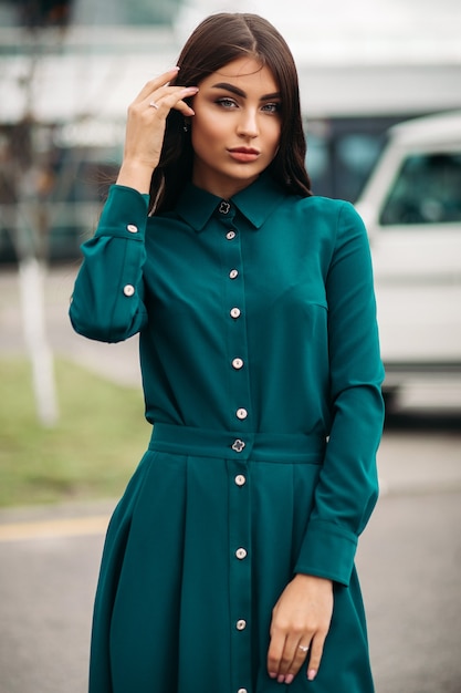 Belle jeune femme aux longs cheveux bouclés portant une robe élégante tout en posant à la caméra à l'extérieur. Concept de mode de vie