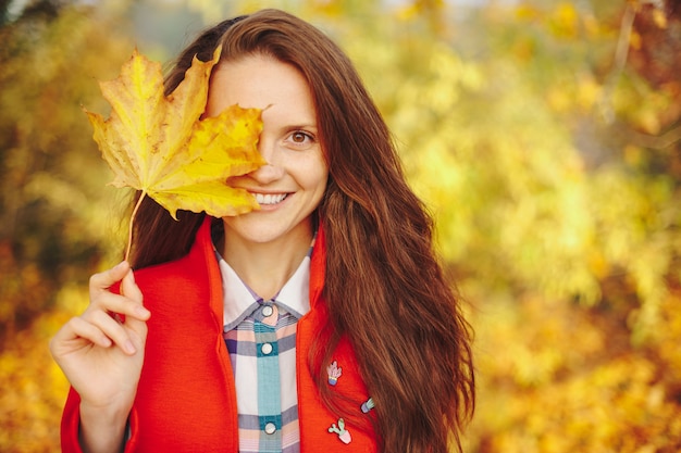 Belle jeune femme aux longs cheveux ondulés couvrant le visage avec une feuille