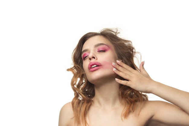 Belle jeune femme aux longs cheveux soyeux ondulés, maquillage naturel avec la main près du menton isolé sur mur blanc. Modèle avec maquillage naturel.