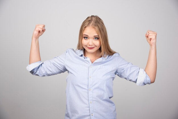 Belle jeune femme blonde debout et montrant le muscle du bras.