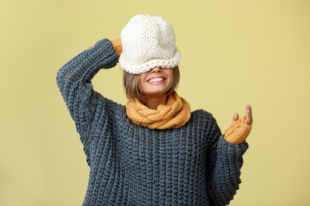 Belle jeune femme blonde en écharpe en tricot chapeau et mitaines posant sur jaune.