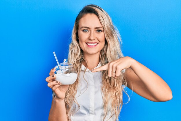 Belle jeune femme blonde tenant un bol avec du sucre souriant heureux pointant avec la main et le doigt