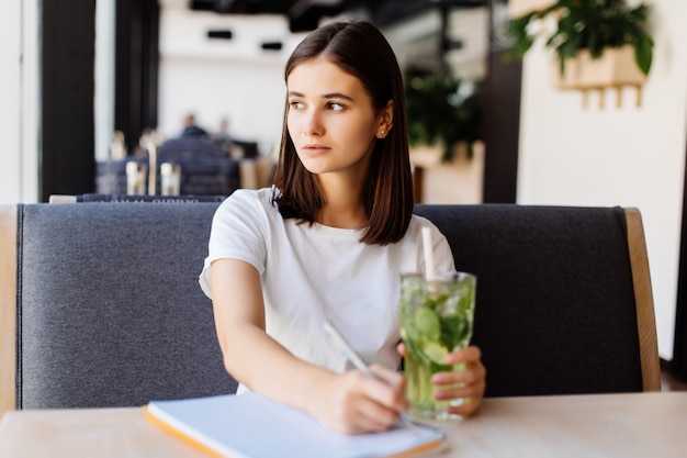 Belle jeune femme boit de la limonade au café