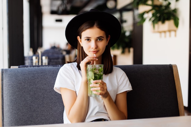 Belle jeune femme boit de la limonade au café