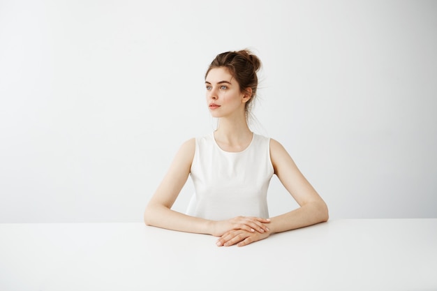 Belle jeune femme brune assise à table directement sur fond blanc.