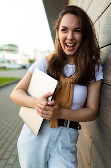 Belle jeune femme brune heureuse à la recherche de côté dans la rue avec un ordinateur portable en mains avec