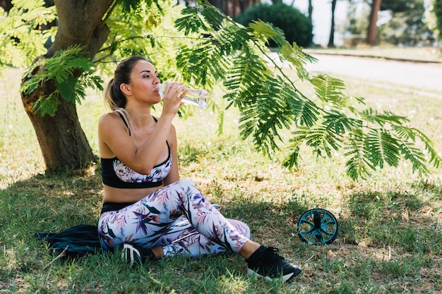 Belle jeune femme buvant de l'eau de bouteille dans le parc