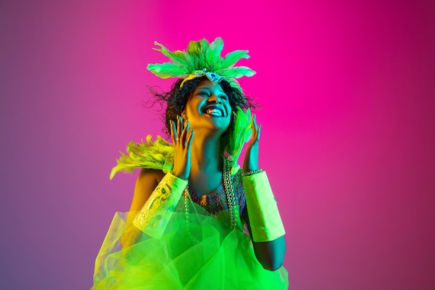 Belle jeune femme en carnaval, costume de mascarade élégant avec des plumes dansant sur un mur dégradé en néon